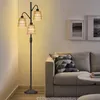 A floor lamp with three rattan shades stands next to a sofa in a living room. Náhľad obrázku produktu
