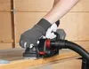 A person wearing gloves is using a cordless planer on a wooden surface, with a vacuum hose attached. Produktbild-Vorschau