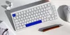 A white mechanical keyboard with blue accents, along with a white mouse, wireless earbuds, and a pen, arranged on a white surface. Produktbild-Vorschau