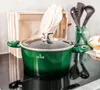 A green pot with a glass lid sits on a black stovetop, with kitchen utensils and a wooden crate in the background. Produktbild-Vorschau