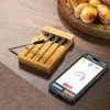 A meat thermometer set and a smartphone displaying an app are on a wooden surface, with cooked potatoes in the background. Podgląd zdjęcia produktu