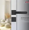 A close-up view of a black door handle and lock set on a white door, with a blurred background of a room interior. Produktbild-Vorschau