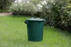 A green trash can sits on a grassy lawn with a bush in the background. Podgląd zdjęcia produktu