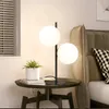 A bedside table with a lamp and a plant next to a bed. Náhľad obrázku produktu