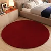 A dark red round rug is placed on a light wood floor in front of a bed and nightstand.