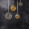 Four clear glass Christmas ornaments filled with fairy lights hang from white ribbons against a dark, textured background. Produktbild-Vorschau
