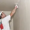 A man is plastering a wall and ceiling with a trowel. Produktbild-Vorschau