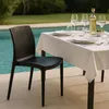 A black chair is placed next to a table set for a meal outdoors, with a swimming pool in the background. Produktbild-Vorschau