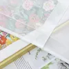 A close-up view of a white sheer curtain with a floral pattern visible underneath, layered over framed artwork. Produktbild-Vorschau