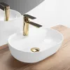 A white oval basin sink with a gold faucet, placed on a wooden countertop. Náhled obrázku produktu