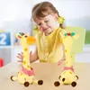 Zwei gelbe Plüsch-Giraffenspielzeuge mit rosa Tupfenschals auf einem Tisch, ein lächelndes Kind im Hintergrund Podgląd zdjęcia produktu