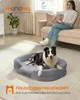 A woman sits on a couch reading a book while a dog rests in a dog bed in the foreground. Produktbild-Vorschau