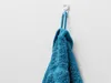 A blue towel hanging on a white hook against a white wall. Anteprima dell’immagine prodotto
