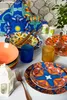 A table setting with colorful plates, bowls, glasses, and cutlery, along with decorative items like a lantern and salt and pepper shakers. Anteprima dell’immagine prodotto