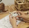 Hands assembling a wooden model kit, likely a classical gramophone, with instructions spread out. Náhľad obrázku produktu