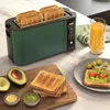 A toaster with four slices of toast in it, placed on a kitchen counter next to a glass of orange juice, avocado, and toast with avocado and tomato. Anteprima dell’immagine prodotto