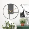 A modern wall clock is displayed on a white wall next to a framed black and white poster. A green shelf below holds potted plants and a decorative deer figurine. Produktbild-Vorschau