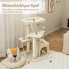 A beige cat tree with multiple levels and platforms, set up on a fluffy white rug in a room with light-colored walls and curtains. A decorative pillow with a cat face is placed next to the cat tree. Náhľad obrázku produktu