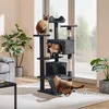 Three Siamese cats are interacting with a multi-level cat tree in a well-lit room with plants and furniture. Produktbild-Vorschau