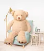 A large teddy bear sitting in a chair next to a lamp and small tables. Produktbild-Vorschau