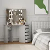 A vanity table with a lighted mirror and makeup products is set up in a bedroom next to a bed. Voir les images du produit