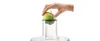 A hand is placing a green apple into a clear cylindrical attachment on what appears to be a kitchen appliance. Náhľad obrázku produktu