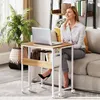 A woman is sitting on a couch next to a small rolling desk with a laptop on it. Anteprima dell’immagine prodotto