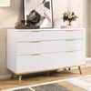 A white dresser with gold accents and wooden legs, decorated with a record player, a framed picture, and a vase of flowers. Podgląd zdjęcia produktu