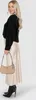 A woman is posing for a product shot, wearing a black sweater, a beige satin skirt, and black ankle boots. She is holding a beige handbag. Produktbild-Vorschau