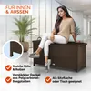 A woman is sitting on a brown storage box in a modern indoor setting with large windows. Produktbild-Vorschau