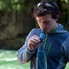 A man is filtering water with a Sawyer MINI water filter into a blue water bottle. Produktbild-Vorschau