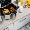 An air fryer filled with french fries and chicken nuggets sits on a kitchen counter next to a glass of milk and a small bowl of seasoning. Náhľad obrázku produktu