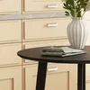A close-up view of a round black table with a folded napkin and a vase with flowers, set against a backdrop of cream-colored kitchen cabinets. Produktbild-Vorschau