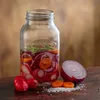 A Kilner fermentation jar filled with sliced red onions, radishes, and carrots, with some whole radishes and sliced carrots and salt scattered on a wooden surface. Podgląd zdjęcia produktu