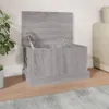 A grey wooden storage chest with its lid open, placed on a wooden floor next to a plant and a sofa. Produktbild-Vorschau