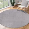 A round gray rug is placed on a wooden floor in a room with a large window and a chair. Náhled obrázku produktu