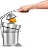 A hand is pressing down on a lever to juice an orange in a silver electric juicer. Náhled obrázku produktu
