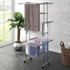 A multi-tiered drying rack with towels and laundry basket in a room with a large window and plant. Náhľad obrázku produktu