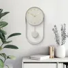 A minimalist pendulum wall clock is displayed on a white wall above a white console table. Voir les images du produit