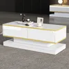 A modern white and gold coffee table with decorative items on top, placed on a grey carpet in a living room setting. Produktbild-Vorschau