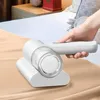 Weißer Handstaubsauger, der von einer Hand von seiner Ladestation auf einer beigen Bettdecke angehoben wird Anteprima dell’immagine prodotto
