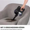 A hand is using a black and blue handheld vacuum cleaner to clean dirt from a gray armchair. Produktbild-Vorschau