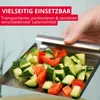 A hand is using a metal scoop to transfer chopped vegetables (cucumber and red bell pepper) from a metal tray. Produktbild-Vorschau