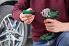 A person is holding a cordless impact wrench and a socket wrench attachment, with a car wheel in the background. Náhľad obrázku produktu