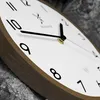 A close-up, angled view of a modern wooden wall clock with a white face and black numbers and hands. Voir les images du produit