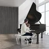 A woman and a baby are sitting on a piano bench in front of a grand piano, with a large window in the background. Produktbild-Vorschau