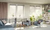 A living room scene with a sofa, armchair, coffee table, plants, and a bookshelf. Produktbild-Vorschau