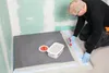 A person is applying sealant to a shower floor. Produktbild-Vorschau