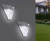 Two triangular solar-powered outdoor lights are mounted on a gray wall, with a house and garden visible in the background. Produktbild-Vorschau