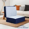 A blue and white folding mattress is placed on a woven rug in a living room setting, with a sofa and pillows in the background. Voir les images du produit